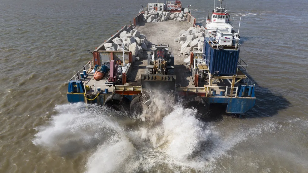 Heavy load digger dropping Armourstone boulders into the water from the SeaRock barge