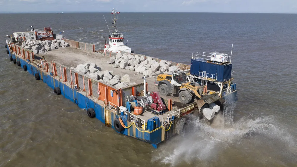 Heavy load digger dropping Armourstone boulders onto the Blue Anchor coast from the SeaRock barge