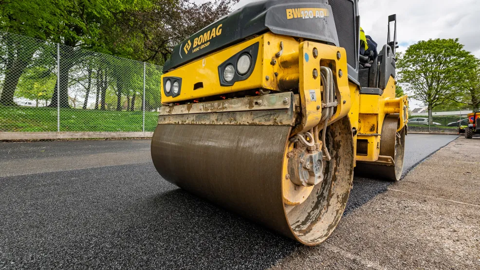Roller compressing and flattening fresh asphalt onto the new tennis court