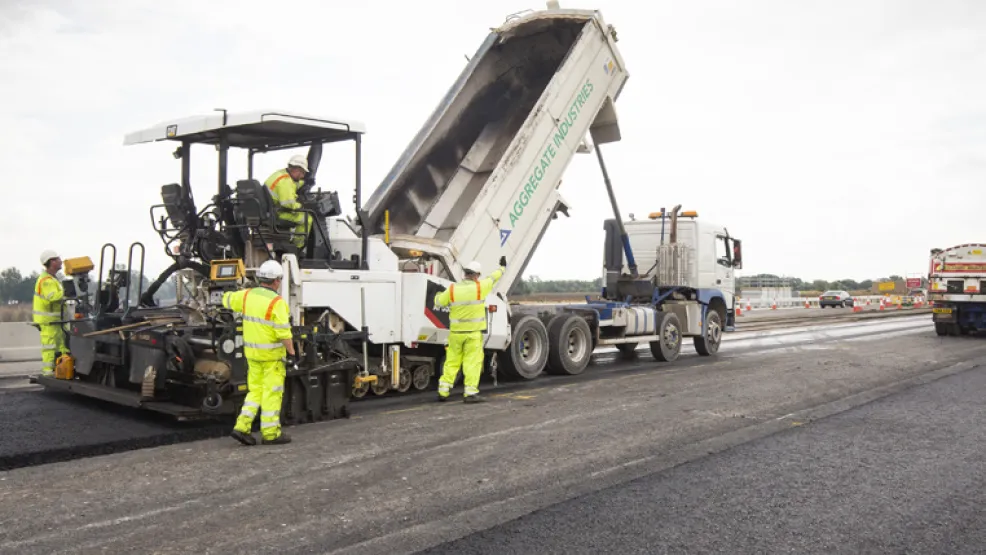 Tipper truck unloading asphalt into a paver on the A14