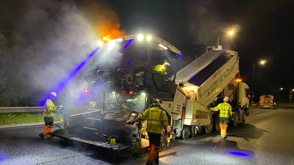 SuperCurve Asphalt being poured into a paver that's surfacing a road at night with workers around