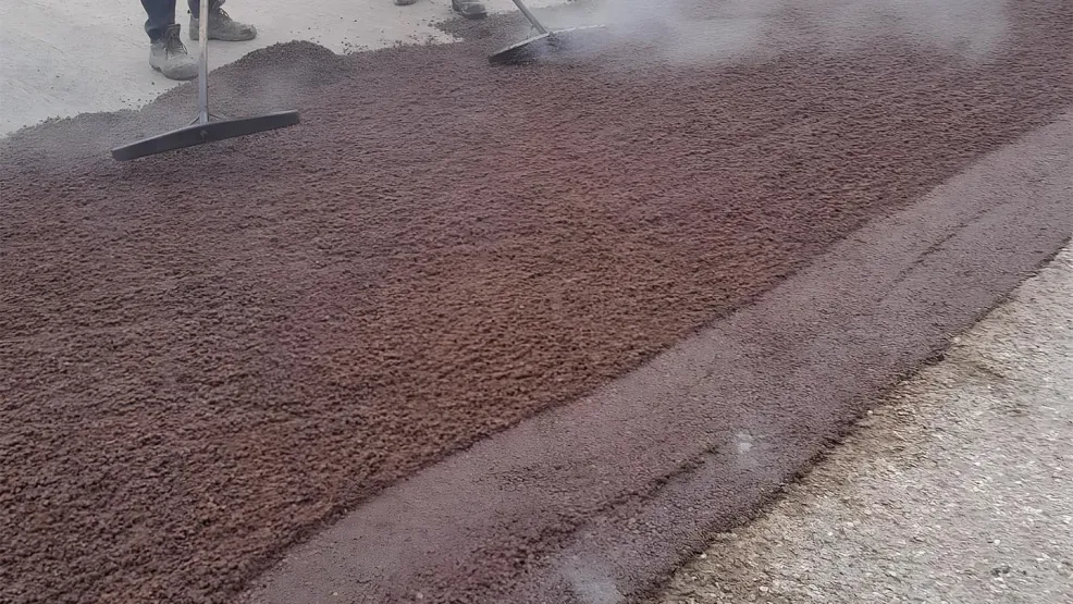 Two workers moving the supercolour ultra asphalt into position with brooms