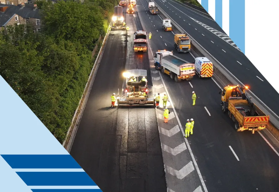 Asphalt construction work being carried out on a motorway with branding graphics around the outside