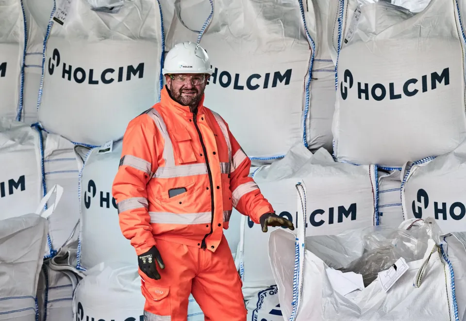 Worker wearing PPE standing in front of large heavy duty aggregate sacks with the holcim logo