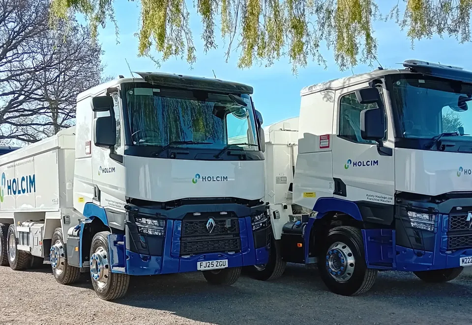 several asphalt trucks under a tree with the Holcim logo
