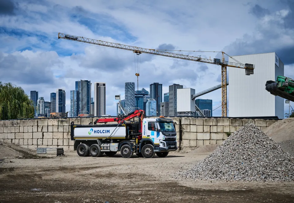 Truck with Holcim branding in a yard with piles of aggregates and the london skyline behind