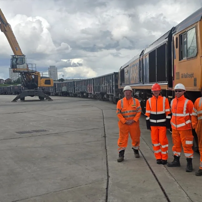 Holcim representatives with partners involved in new rail route from Bardon to Sunderland in high viz PPE in front of a freight train.