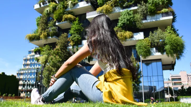 Girl sitting on the grass in front of green growth multi-storey building