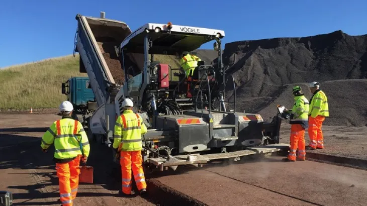 Roller Compacted Concrete being laid by a paver and workers