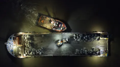 Top down image of the SeaRock barge being moved into position by a tug boat at night