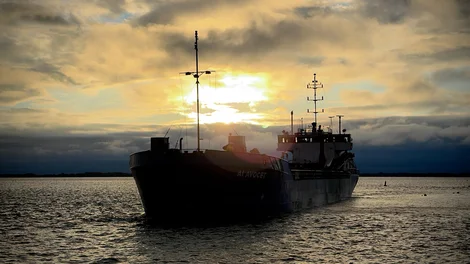 Large aggregate ship on the open water silhouetted by a golden sunset through the clouds
