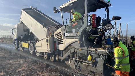 A paver lays CBGM on the M42 Motorway as a workmen ion high viz PPE watches on