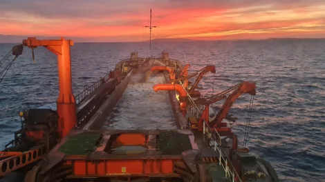 Water being pumped onto aggregates ship at sunset on the open ocean