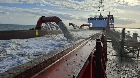 Water is being pumped into the storage area of an aggregate haulage ship on the open water