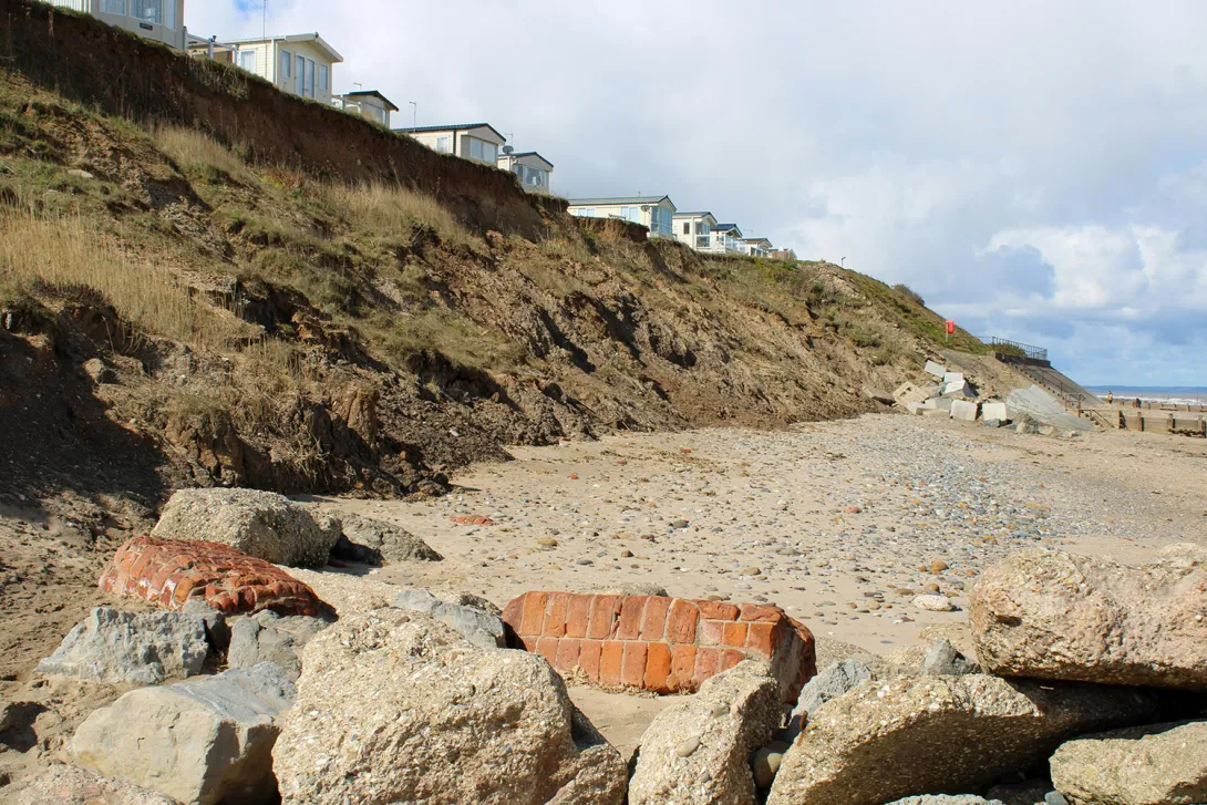 Small houses along a cliff edge, leading to a rocky beach at the sea