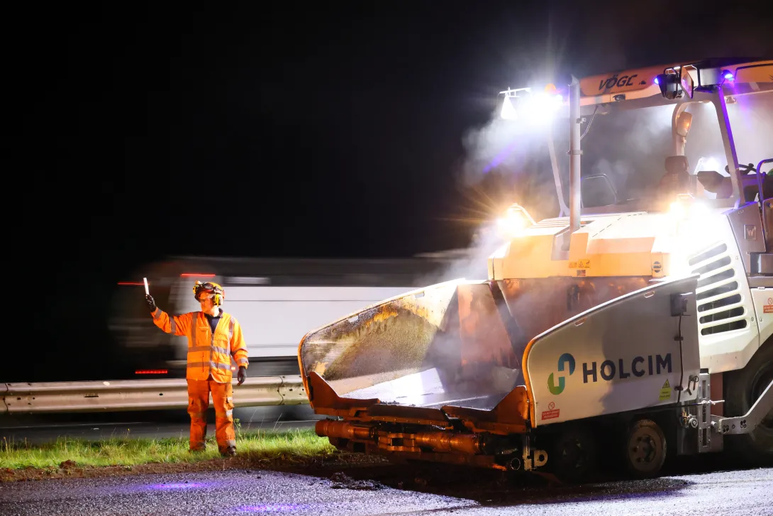 A workman in high viz PPE observes as a Holcim vehicle works on the M5 motorway at night