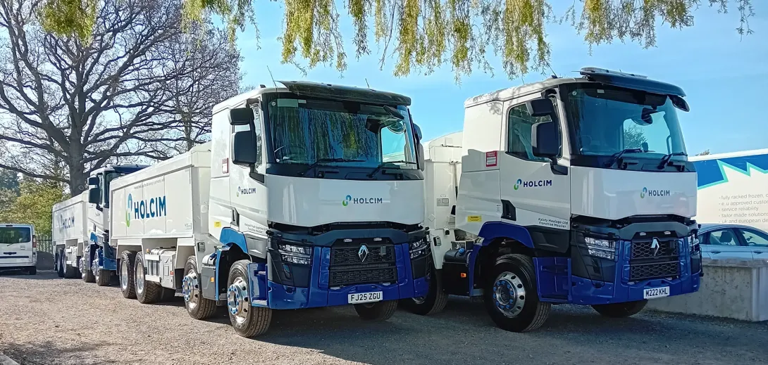 several asphalt trucks under a tree with the Holcim logo