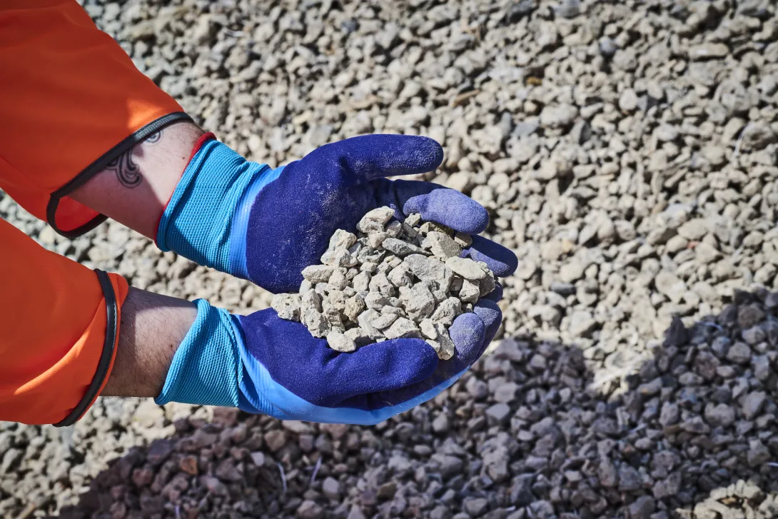 A worker wearing blue gloves holds a handful of construction demolition materials following processing