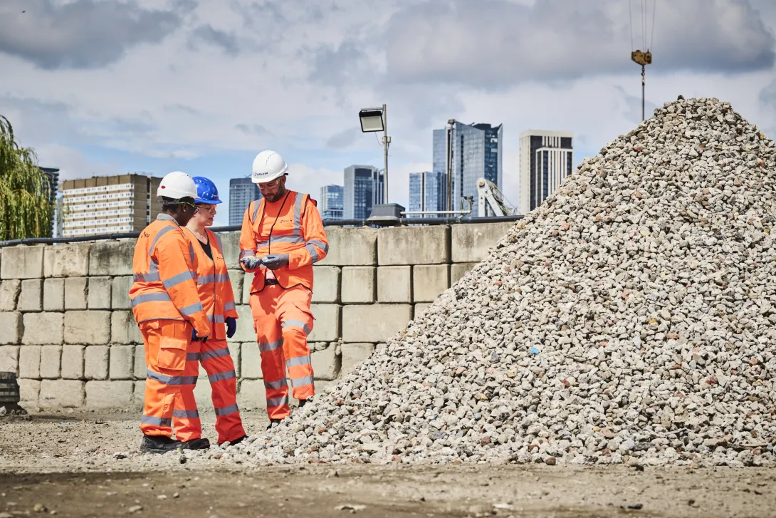 Three Holcim colleagues in high visibility orange PPE survey processed materials at the Morden Wharf Recycling Centre in London