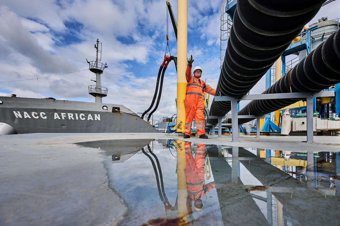 A Holcim UK team member in high viz PPE next to a pipe discharging materials from the Naac African ship at the Tilbury Cement site