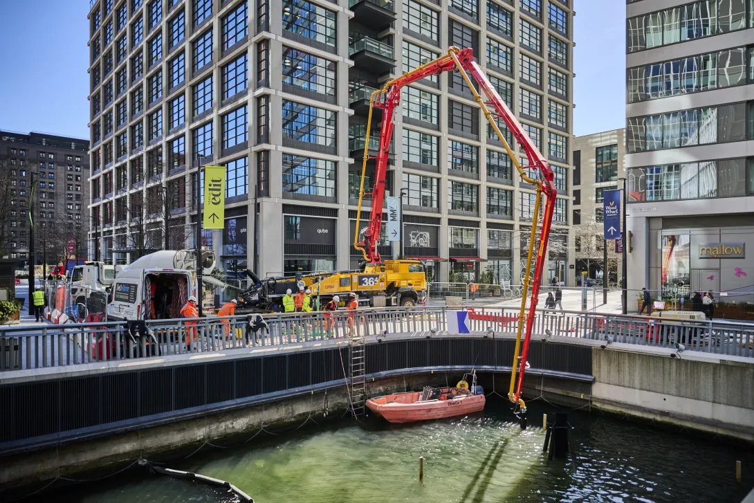 A Holcim UK mixer truck pours biochar coffee concrete into pumping equipmet at Canary Wharf. The product was developed to support The Whale on the Wharf sculpture, which is is made of recovered plastic ocean waste.