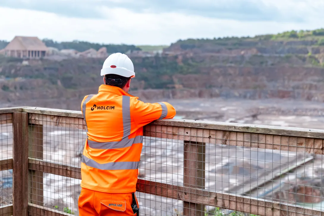 A male worker in Holcim high visibility PPE looks out over Torr Quarry floor from a viewing platform