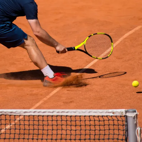 Tennis play with racket skidding through sand to reach the ball