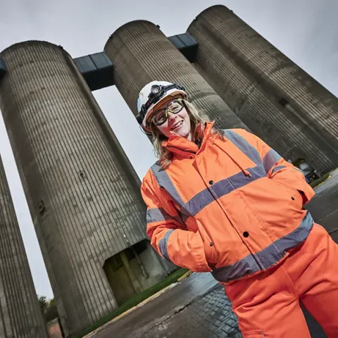 Lady in PPE standing in front of cement silos