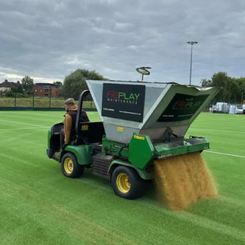 A machine spresding specialist sports sand on a new synthetic pitch at Oasis Academy in Croydon